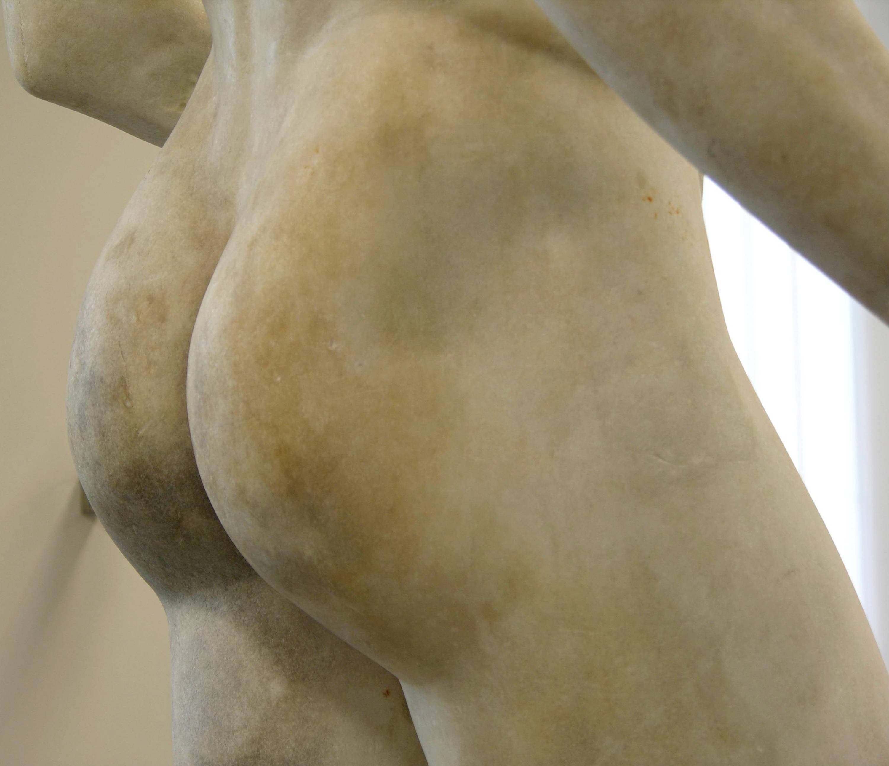 Nahaufnahme des unteren Rückens und des Gesäßes einer Marmorstatue, die die glatte Textur und die natürlichen Farbvariationen des Steins zeigt.
