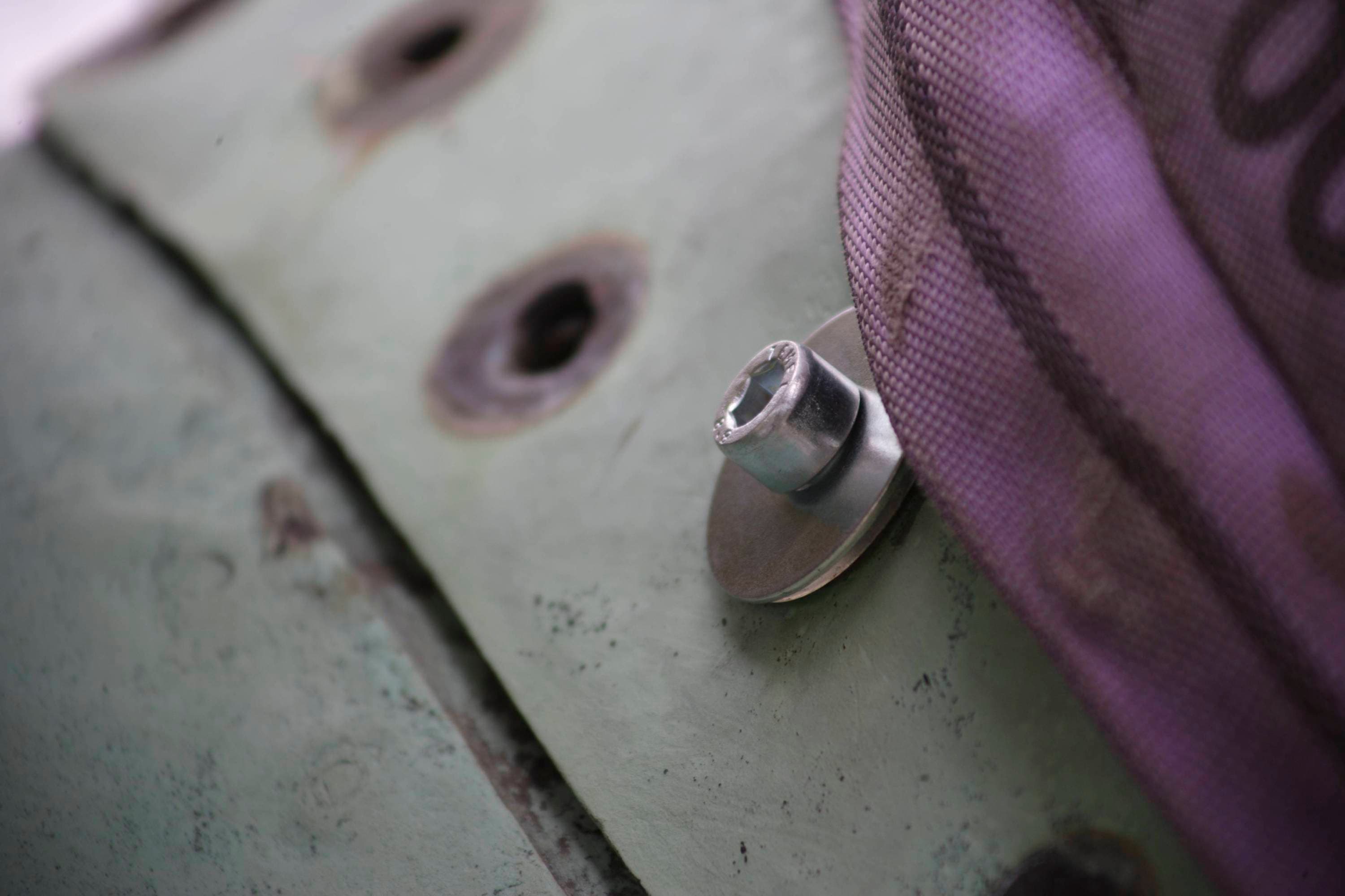 Nahaufnahme einer Metallschraube mit Unterlegscheibe, die an einer grünen Oberfläche befestigt ist, neben einem violetten Stoffband.